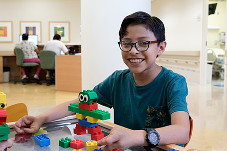 Paciente con playera verde y lentes sosteniendo figuras de legos