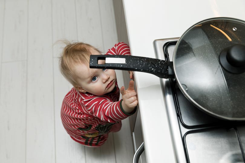 Small child looking up at pan handle on stove