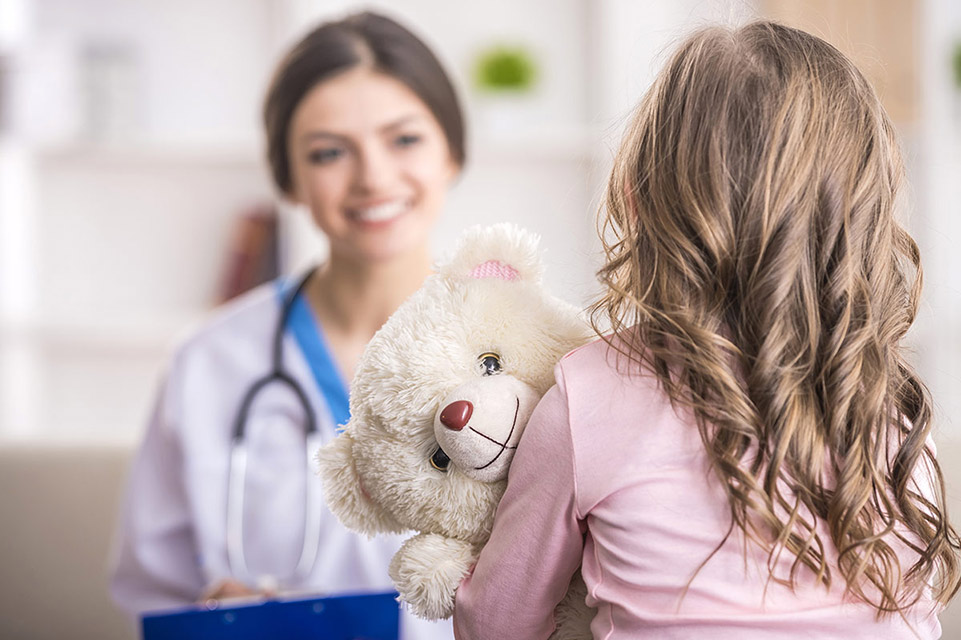 Female doctor and girl holding her teddy bear at doctor visit 