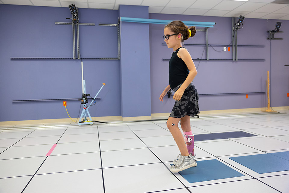 female patient with leg brace walking with motion analysis trackers placed on her limbs