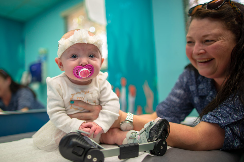 clubfoot patient in boots and brace, staff member smiling