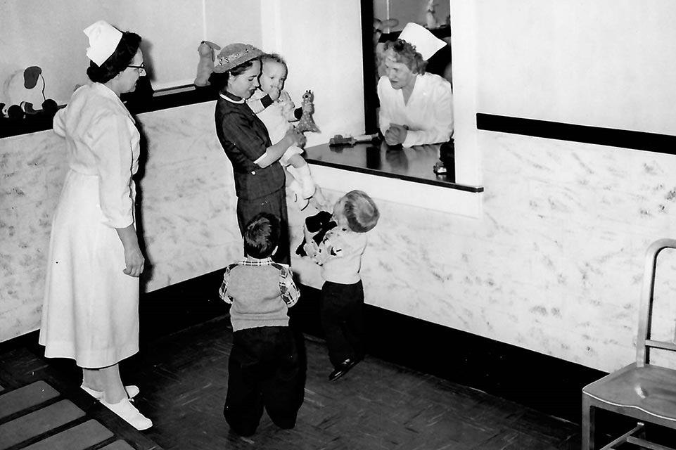 madre registrando a un paciente en la década de 1940, tres niños y dos miembros del personal