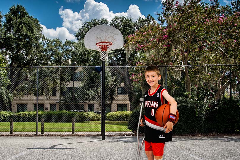 Niño con muletas sosteniendo un balón en una cancha de baloncesto.