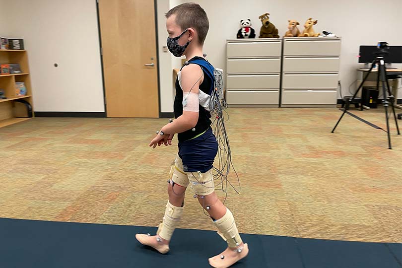 Niño caminando sobre una alfombra con sensores en las piernas y el cuerpo.