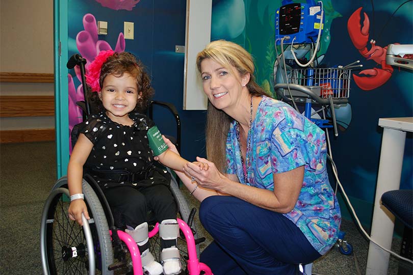 Enfermero arrodillado junto a una niña en silla de ruedas.