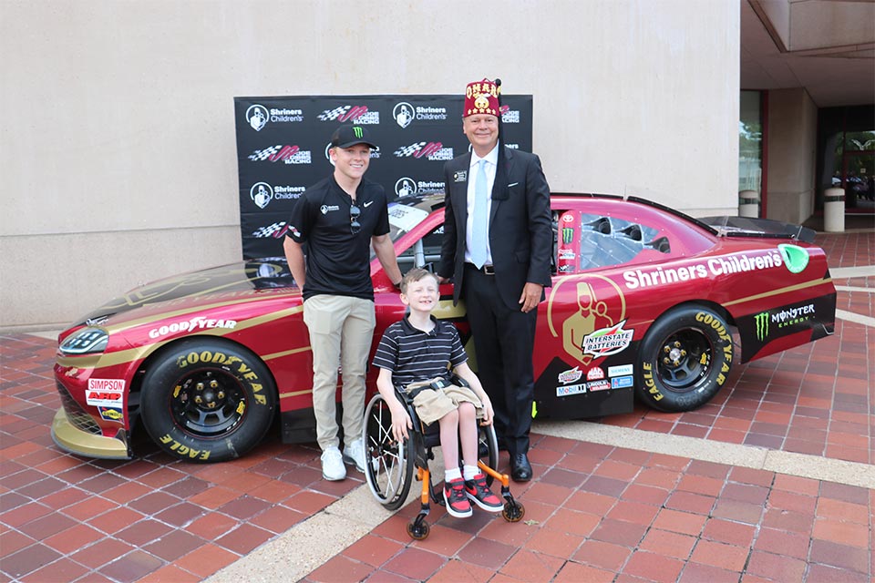 Ty Gibbs standing next to his racecar with Kenny Craven and a patient
