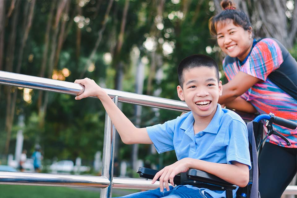 Varón joven en silla de ruedas en el parque con su madre a su lado