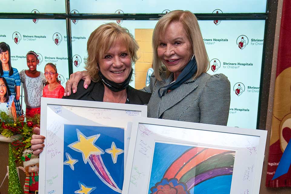 Marcia with friend, both holding artwork