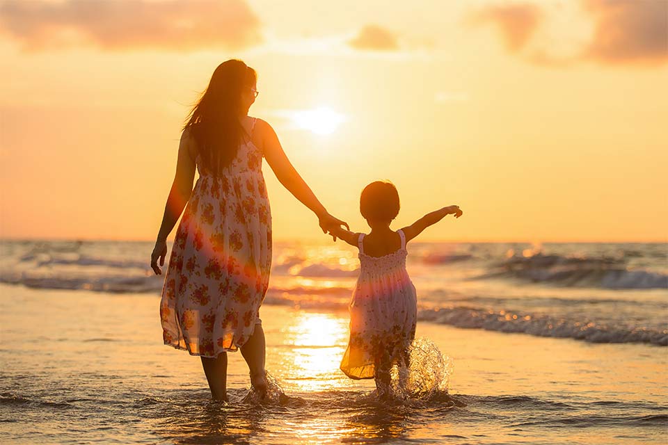 Mother and daughter walking in water at beach at sunset