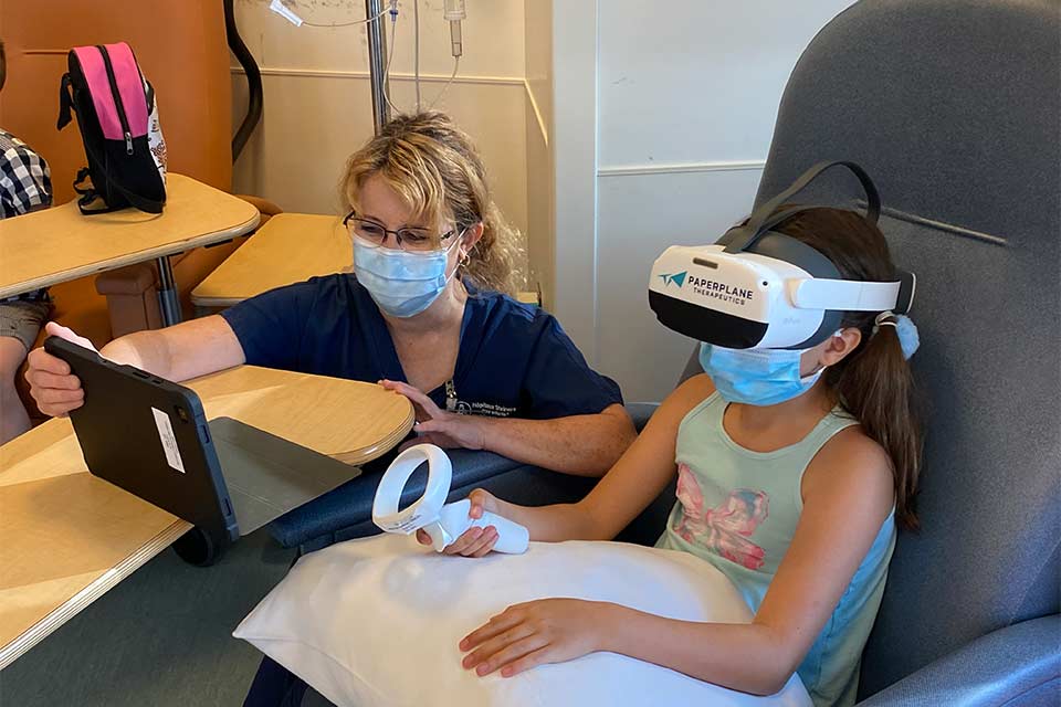 Female patient wearing virtual reality helmet next to female child life specialist
