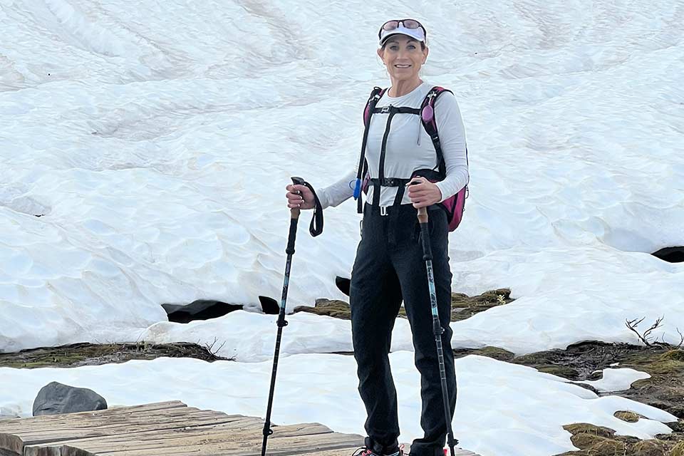 Lynda de pie junto a una montaña cubierta de nieve sosteniendo bastones de senderismo