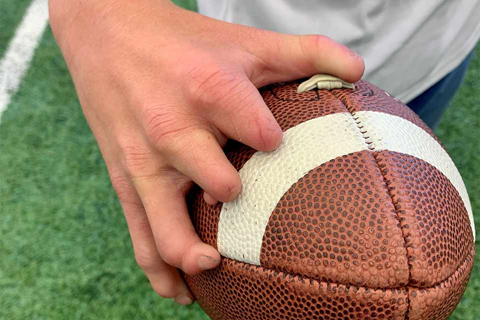 La mano derecha de una persona con diferencias en los dedos sosteniendo un balón de fútbol.
