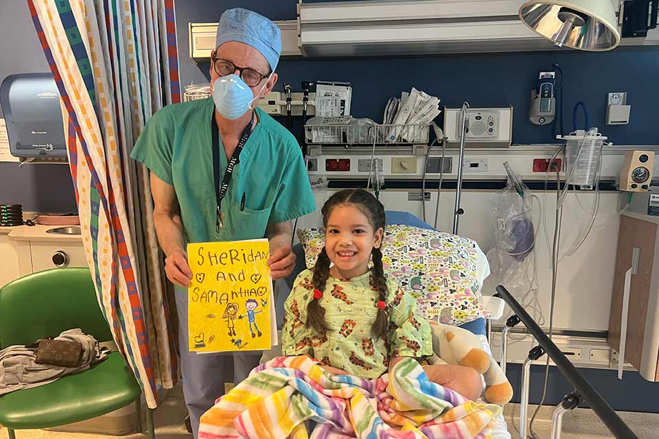 Le Dr Sheridan tenant un dessin à côté d’un lit d’hôpital avec une patiente