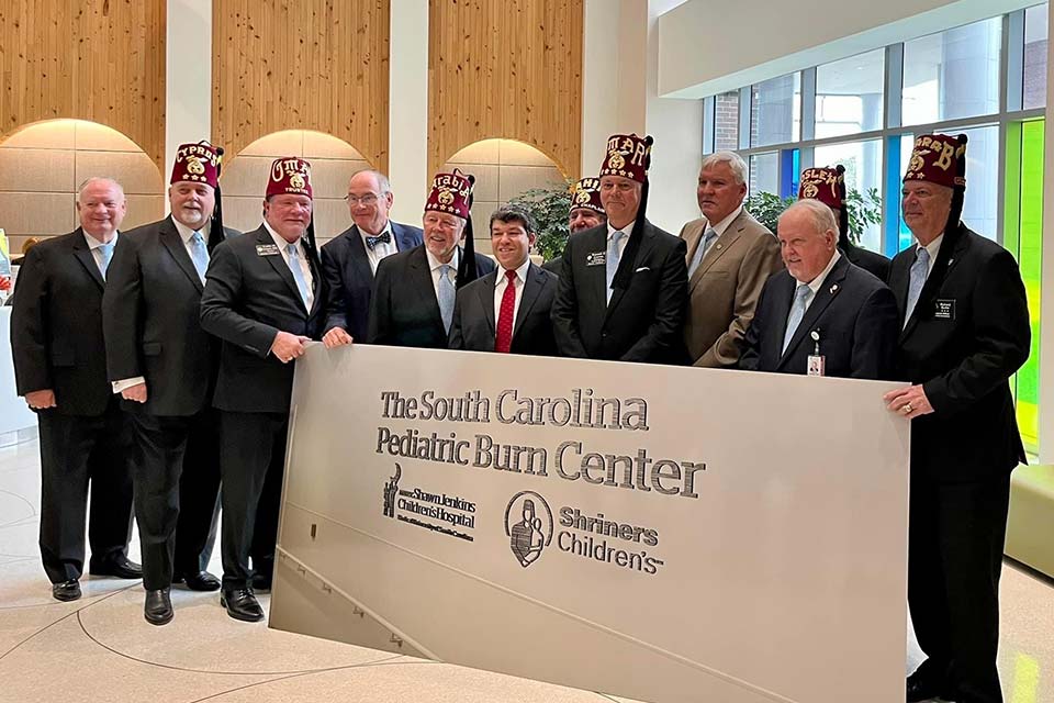 Des membres de Shriners International et des dirigeants du MUSC se tenant devant le panneau du Centre de traitement des brûlures