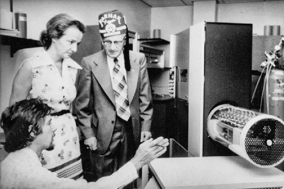 Historic image of three people viewing lab equipment