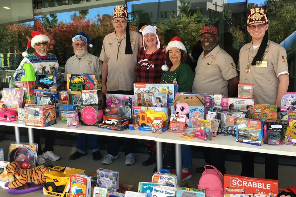 Shriners and volunteers in front of table loaded with toy donations