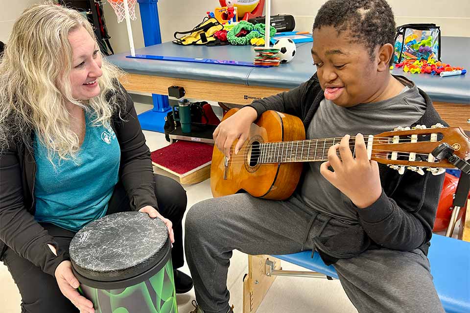 child life specialists plays drums with patient that is playing guitar
