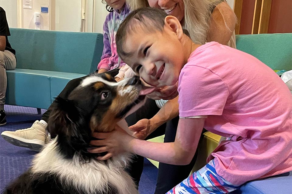 Un chien de thérapie embrasse le visage d'une patiente en chemise rose