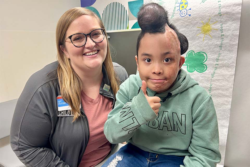 child life specialist poses with patient giving a thumbs up