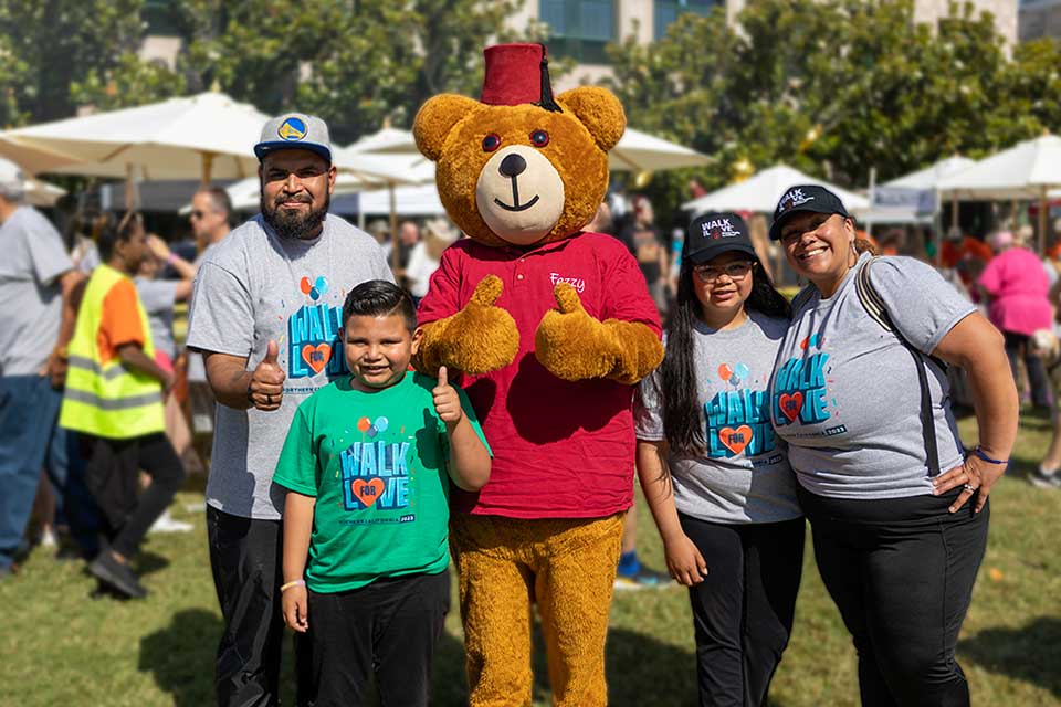 mother, father, daughter, and son in Walk for Love shirts posing with Fezzy bear