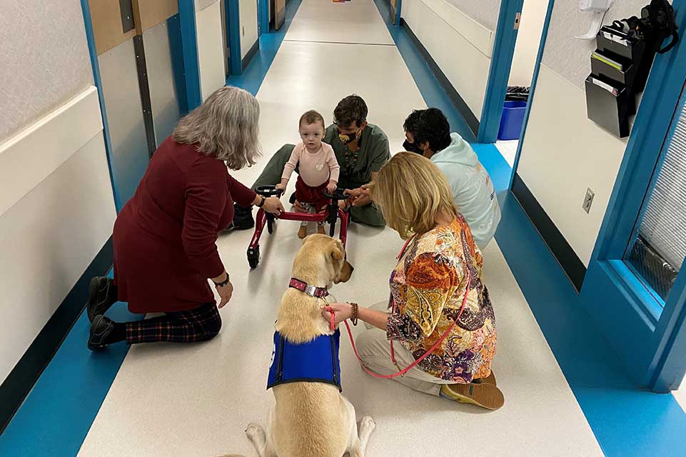 Jaslynn usando un andador con miembros del personal y un perro de terapia
