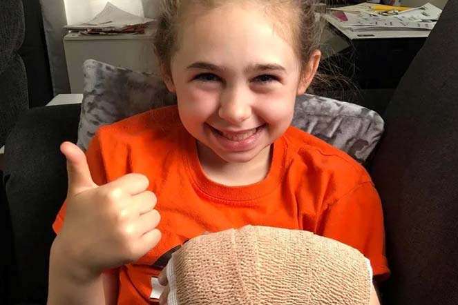 Maddie giving a thumb's up with bandage on left hand
