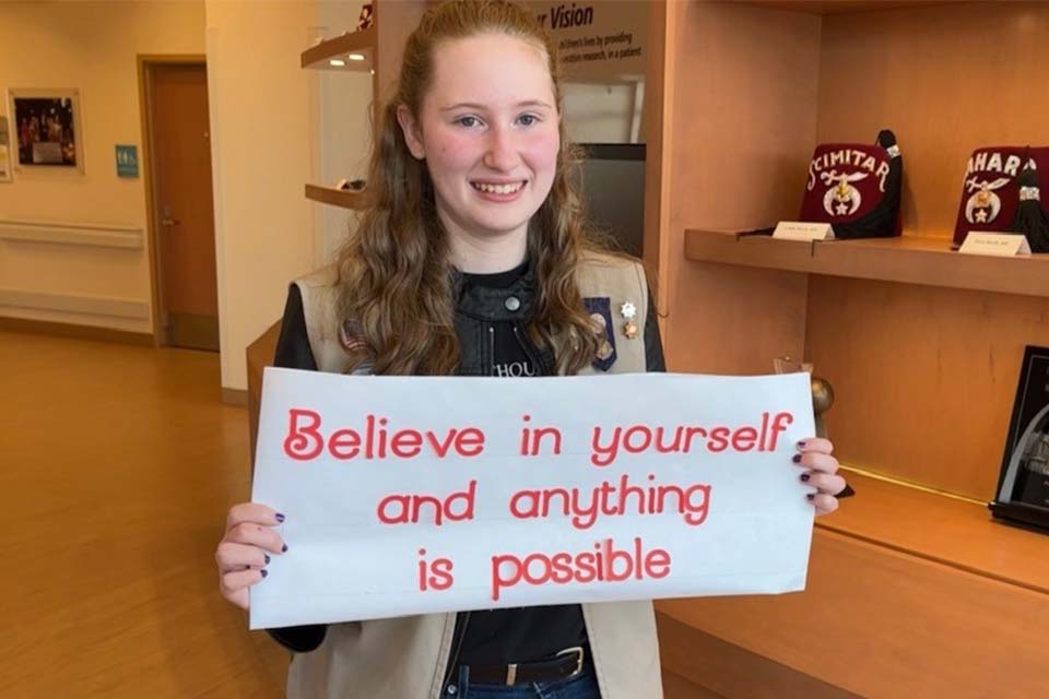 Julie sosteniendo un cartel blanco con una cita que dice “Cree en ti mismo y todo será posible”