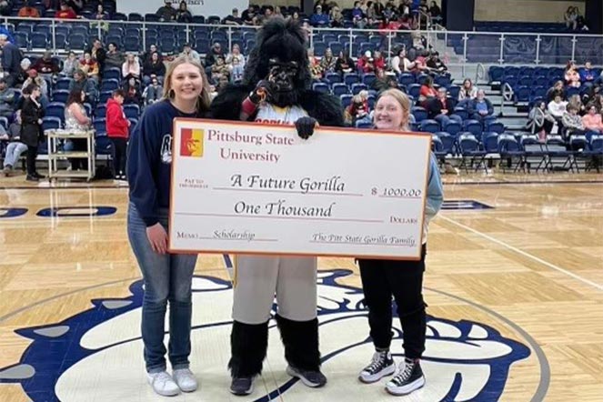 Malorie with another student and mascot on gym court holding a large check