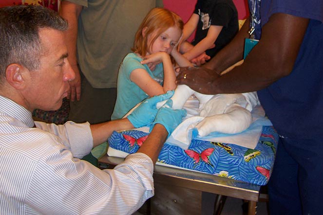 Un médico examina el pie del bebé Keoni mientras su hermana observa
