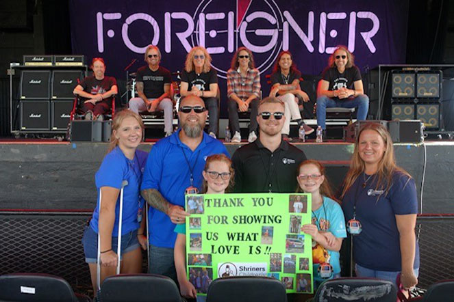 Faith, her family and Foreigner band members, Faith holding sign reading "Thank you for showing us what love is"