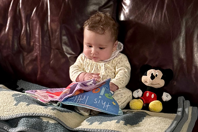 patient reading baby book on couch with toy and blanket