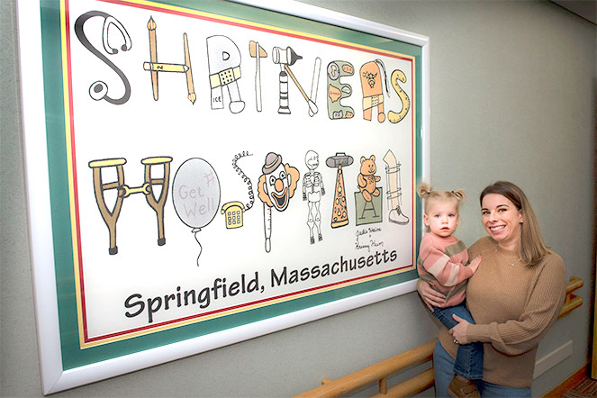 Krissy with daughter in front of Shriners Hospital Springfield, Massachusetts, sign she designed