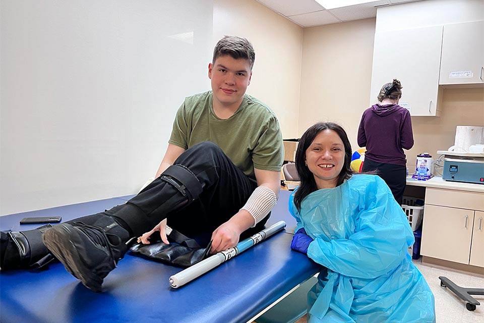 Ivan with leg brace sitting on table, physical therapist standing next to him