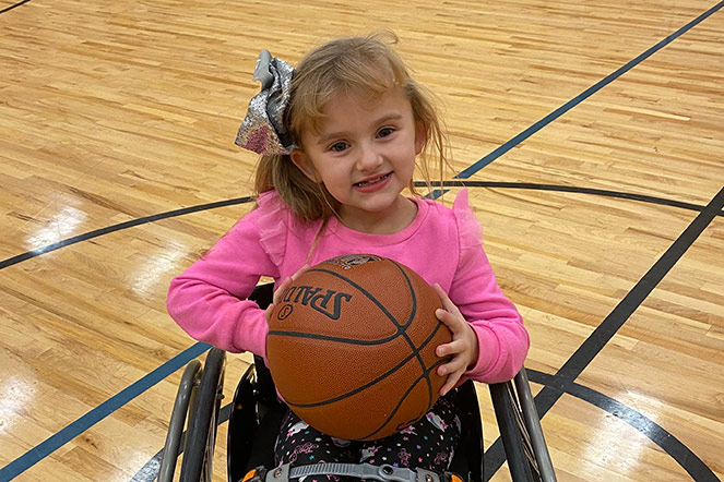 Hadley sosteniendo una pelota de básquetbol en la cancha, sentada en una silla de ruedas.