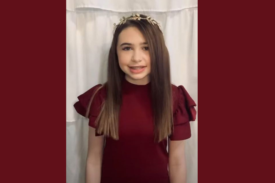 Maddie en robe rouge, debout devant un rideau, avec une couronne sur la tête