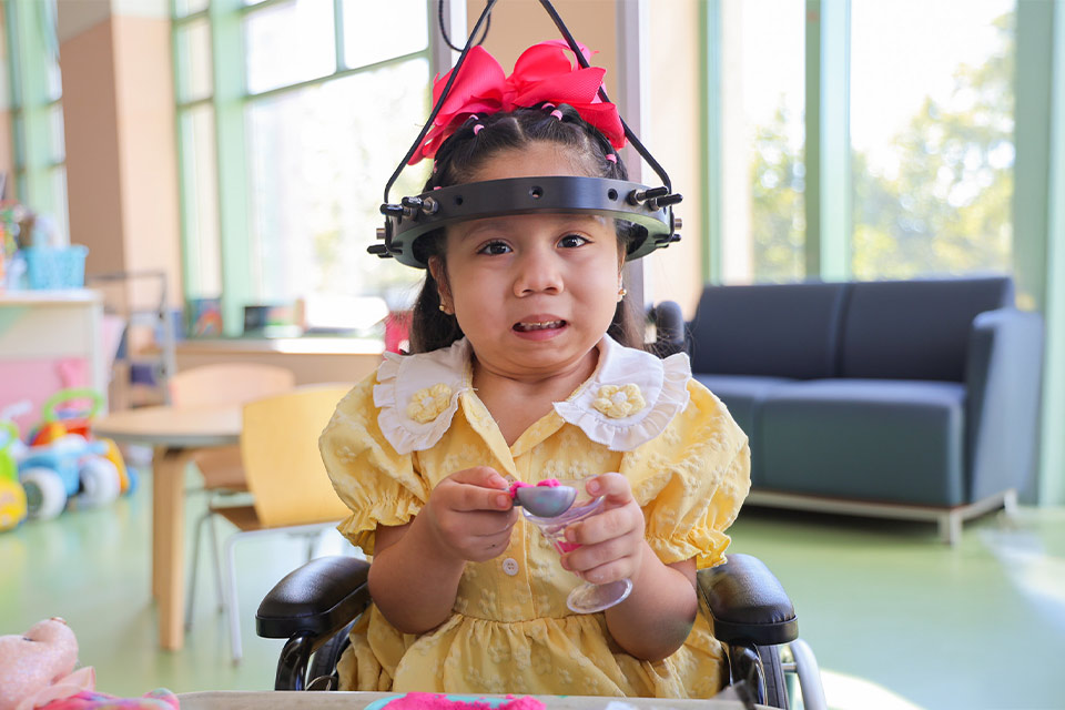 a patient in a yellow dress wearing a halo gravity traction device holding a plastic tea cup