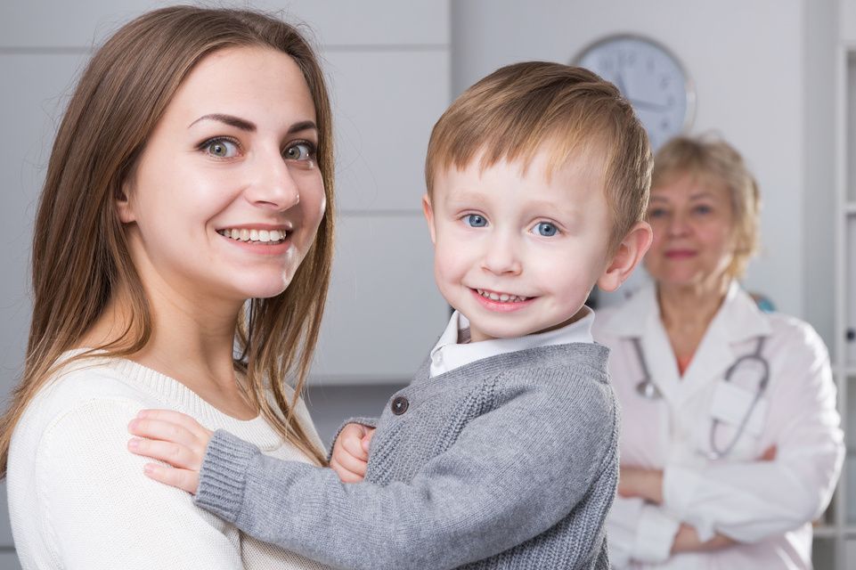 mom holding toddler while physician looks on