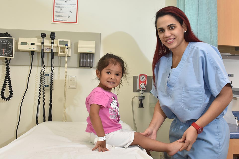 Doctora sosteniendo pierna de paciente de short color blanco y blusa color rosa