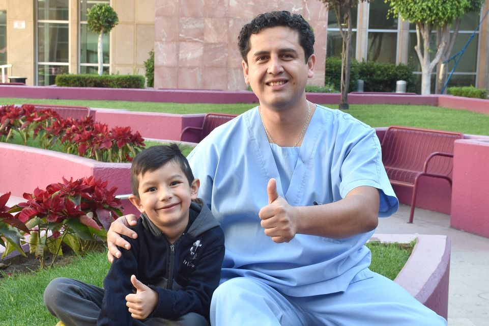 Doctor Clemente con paciente de suéter color azul marino ambos levantando el dedo pulgar  