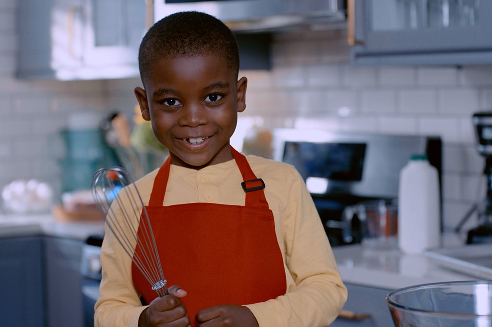 Little boy holding a whisk in a kitchen